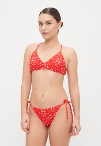 Rød bikini med hvit blomsterdesign, med trekantet topp og justerbare båndsider. Glatt stoff med en lett glans.