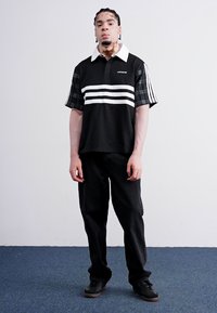 Black polo shirt featuring white horizontal stripes, contrast checked sleeves, and a white collar. Paired with black pants and sneakers.