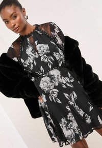 Juoda gėlėta suknelė su permatomu nėrinių dekolte, papuošta perlų ir nėrinių detalėmis. Derinama su juoda dirbtinio kailio striuke.