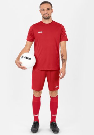 Rotes sportliches Trikot und Shorts mit weißem JAKO-Logo, kombiniert mit roten Socken. Der Spieler hält einen weißen Fußball und zeigt eine sportliche Erscheinung.