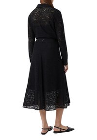 Schwarzes Spitzenkleid mit langen Ärmeln, komplizierten Blumenmustern und einem ausgestellten Rock, der unter die Knie fällt. Enthält eine taillierte Taille und flache Schuhe.