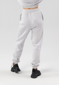 Világosszürke melegítőnadrág rugalmas derékkal, oldalsó zsebekkel és gumis bokákkal, fekete sportcipőkkel párosítva. Simább tapintás.
