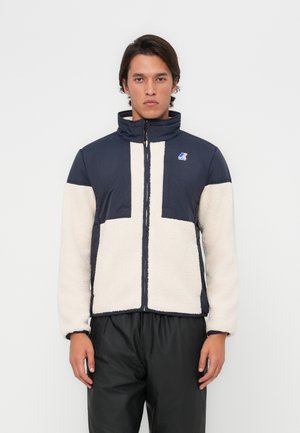 Veste en polaire navy et crème avec fermeture éclair à l'avant, col haut et logo sur la poitrine gauche. Présente un design en blocs et des poignets élastiques.
