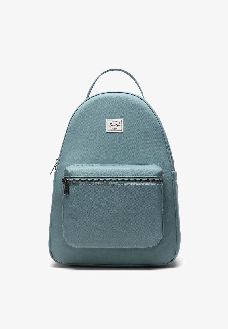 Sac à dos bleu clair avec un dessus arrondi, une poche zippée à l'avant et une texture en tissu. Il comporte un patch étiquette en haut et des bretelles réglables.