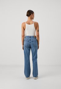 Top de alças branco canelado emparelhado com jeans de denim azul de corte solto e cintura alta, apresentando bolsos de retalho e um efeito desbotado.