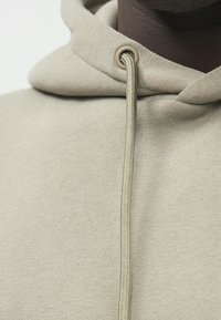 Hettegenser i lys beige stoff med myk tekstur. Har snor med beige hempe og minimalistisk design.