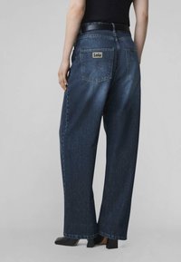 Vaqueros de mezclilla azul oscuro de pierna ancha con cintura baja, dos bolsillos traseros y una etiqueta de la marca con la palabra "Lois".