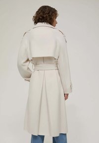 Cappotto bianco con vita cintrata, design doppiopetto e dettagli sulle spalle. Presenta una parte posteriore plissettata e un colletto strutturato.