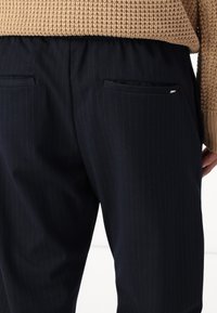 Marintröjda byxor med elastisk midja, som har två bakfickor och en slät yta. Bär en beige stickad tröja.