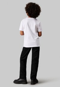 Camiseta de algodón blanca con mangas cortas, combinada con pantalones de mezclilla negros. Zapatos negros con cordones completan el look. Diseño simple y casual.