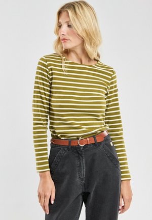 Chemise à manches longues à rayures vert olive et blanches en tissu doux, associée à un pantalon taille haute gris foncé et une ceinture marron.