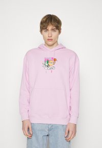 Gaiši rozā kapuce ar priekšējo kabatu, kurai ir krāsains grafiskais dizains uz krūtīm. Izgatavota no mīkstas auduma, ar auklām uz kapuces.