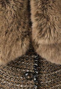 Abrigo de tweed marrón con un suave collar de piel sintética, cierre de botones oscuros y una tela texturizada con manchas de blanco y crema.