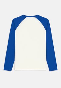 Långärmad skjorta med vit kropp och blå raglanärmar, tillverkad av mjuk bomull. Rund halsdesign med minimala sömnadsdetaljer.