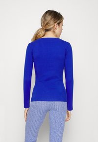 Blaues, geripptes Langarmshirt mit figurbetonter Silhouette, ausgestattet mit einem breiten Ausschnitt und texturierter Stoffstruktur. Kombiniert mit hellblauen, gerippten Leggings.