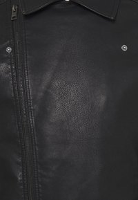 Giacca in pelle nera con finitura testurizzata, dotata di cerniera frontale, bottoni a pressione e design classico del colletto.