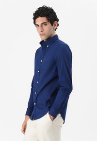 Camisa de botones azul marino, hecha de una mezcla de algodón, que presenta un cuello clásico, botones blancos y un pequeño detalle de logo en el pecho.