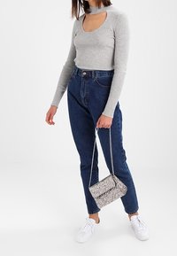 Szary, prążkowany, długorękawowy top z dekoltem w serek, zestawiony z niebieskimi dżinsami z wysokim stanem oraz błyszczącą, srebrną torebką na ramię, posiadającą łańcuszkowy pasek.