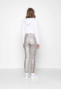 Huva vit sweatshirt med långa ärmar, tillsammans med glänsande silverfärgade läderimitation leggings med ormskinnsmönster, och vita sneakers.