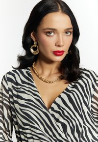 Zebra-Muster Kleid mit schwarz-weißen Streifen und durchsichtigen Ärmeln. Mit einer goldenen Halskette und großen Creolen als Accessoires.