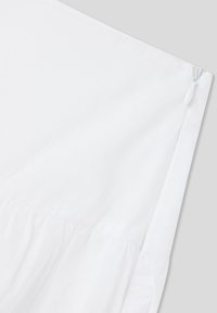 Sezione di tessuto bianco con texture arricciata, dotata di chiusura con zip. Superficie liscia, senza motivi o accenti visibili.