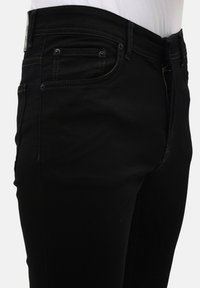 Zwarte denimjeans met een aansluitend ontwerp, voorzien van vijf zakken en subtiele contraststiksels. De stof lijkt glad met een minimale textuur.