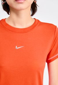 Narancssárga sportpóló sima anyagból, ezüst Nike logóval a mellkasán és rövid ujjakkal, egyszerű varrással.
