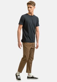 T-shirt grigia, pantaloni a sigaretta marroni, sneakers nere e calzini a fantasia. Design semplice, hardware minimal e look aderente.