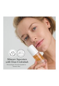 Klare Glasflasche mit weißem Deckel, die ein orangefarbenes Serum enthält. Text hebt "Dermatologisch getestet" und "Geeignet für empfindliche Haut" hervor.