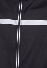 Svart vindjacka med texturerad tyg, med hel dragkedja och två horisontella vita ränder över bröstet för kontrast.