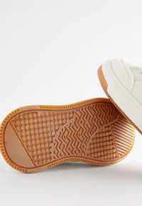 Hvide sneakers med en struktureret gummiydersål i lys brun, der har et blandet mønster af sekskanter og zigzag, samt glatte sideaccentuer.