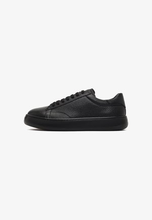 Zapatilla negra de cuero con una superficie texturizada, puntera redonda, cordones planos, cuello acolchado y una suela de goma sólida para ofrecer agarre.