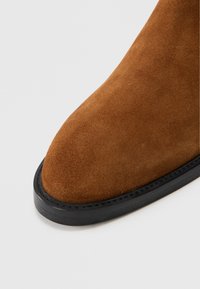 Braune Wildleder-Stiefelette mit runder Zehenpartie, schwarzer Sohle und nahtlosem Design. Die Oberfläche ist glatt mit einem weichen Finish.
