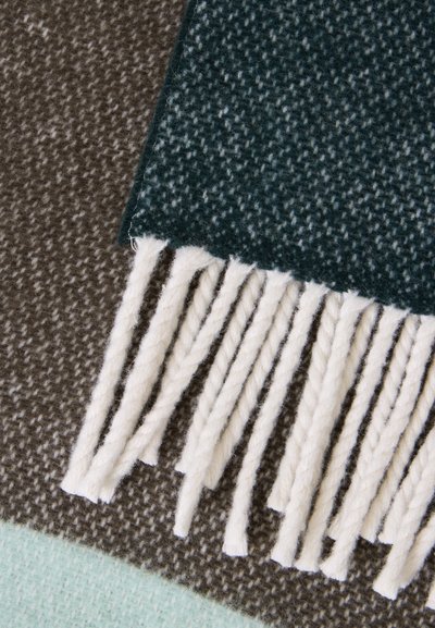 Gros plan d'un tissu en laine vert foncé avec franges sur des tissus tissés marron et bleu clair texturés.