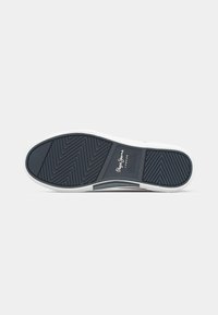 Tengerészeti sneaker talp, textúrált gumimintával, fehér szélekkel és márkázási részletekkel. Cikkcakkos futómintázattal a tapadás és a stabilitás érdekében.