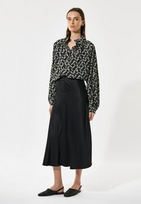 Črna satenasta krila v kombinaciji s črno-belo bluzo z vzorcem listov. Bluza ima dolge rokave in ovratnik. Črne strukturirane slip-on čevlje.