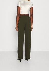 Hoch taillierte, weit geschnittene Hose aus olivgrünem Stoff. Glatte Textur, elegantes Design mit einem verdeckten Bund und minimalistischen Nähten.