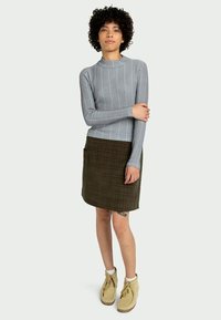 Maglietta a maniche lunghe grigia a costine abbinata a una gonna a quadri verde; la modella indossa stivaletti beige alla caviglia e ha i capelli ricci.