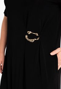 Schwarzes Kleid mit glatter Textur, versehen mit einem goldfarbenen, gedrehten Metallakzent in der Taille und seitlichen Raffungen.