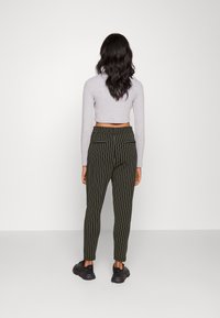 Calças tapered listradas em verde com cintura elástica, combinadas com uma blusa cropped de manga longa cinza claro. Sapatos de desporto pretos usados.