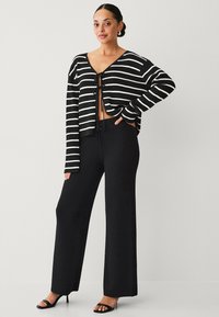 Sort-hvid stribet cropped cardigan med båndlukning. Parret med højtaljede sorte brede bukser. Glat stofstruktur.