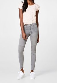 Jean skinny gris avec des panneaux texturés au niveau des genoux, associé à un t-shirt rose pâle avec un imprimé animal discret. Porté avec des baskets blanches.
