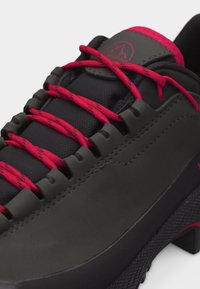 Pantof de drumeție negru și gri închis cu șireturi roșii trecute prin ochiuri tip buclă, cu limbă căptușită și logo montan.