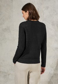 Zwarte gebreide trui met een ronde halslijn, textuurstof en ribbels aan de mouwen, gecombineerd met beige broek.