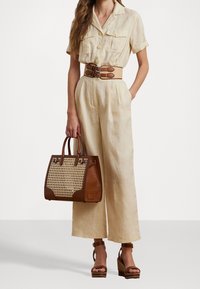 Linnesoverall i ljusbeige, bältad med ett tan-färgat vävt bälte, tillsammans med en brun läderväska med vävda detaljer och klumpiga plattformssandaler.