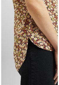 Blusa floreale con base nera, caratterizzata da piccoli fiori bianchi e foglie verdi. Fessure laterali, tessuto morbido e fit rilassato. Abbinata a pantaloni neri.