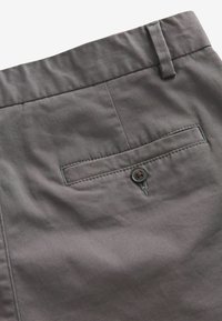 Harmaat kudoshortsit, joissa on sileä pinta, nappikiinnitys takataskussa ja litteä vyötärö. Saumadetailit ovat näkyvissä.