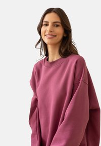 Przesadny sweter z okrągłym dekoltem w głębokim mauve, wykonany z miękkiego materiału o gładkiej fakturze i ściągaczami przy mankietach, zaprojektowany z myślą o komforcie.