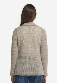 Beżowy sweter z dzianiny o teksturowanym wzorze, z długim rękawem i kołnierzykiem; charakteryzuje się lekko luźnym krojem i dołem, który delikatnie się zaokrągla.