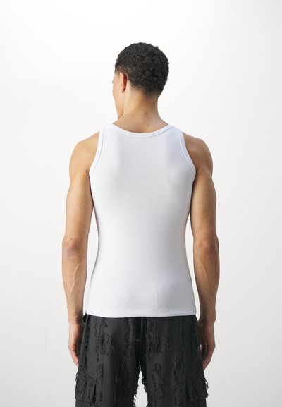 Débardeur blanc à côtes avec un design ajusté, des bretelles étroites et un col rond ; porté avec un short noir texturé.